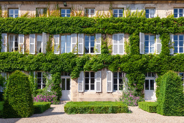 Beautiful antique old brick house rustic window with white wooden shutters, flowers, entwined green ivy covered exterior wall of historic building, in european village