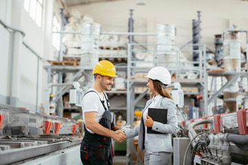 Architect and worker working on project. Colleagues handshaking in factory.	