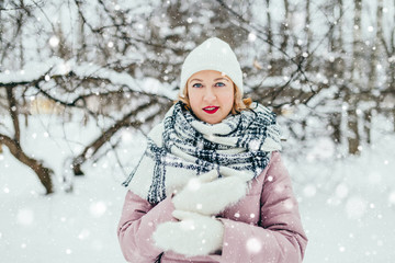 Young attractive blonde in a warm down jacket, knitted mittens, a scarf and a hat in a cold winter forest - warm and cozy clothes