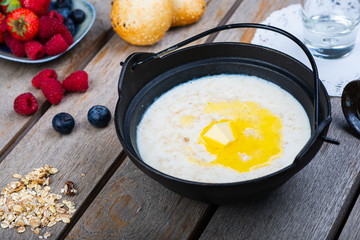 Traditional breakfast milk porridge with butter and berries on a wooden table.