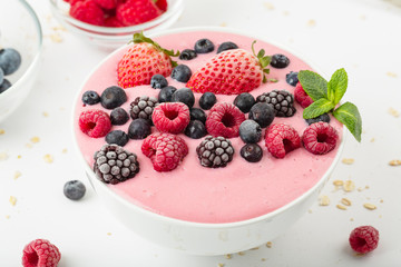 Smoothie bowl with yogurt, muesli and frozen berry. Pink yogurt smoothie bowl topped with frozen berries raspberries, strawberries, blackberries and blueberries. Healthy summer dessert. 