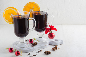 Two glass glasses of mulled red wine with orange slices stand on a white wooden table. On the table...