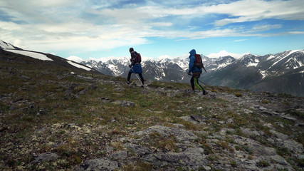 Two tourists walking in the mountains with backpacks and poles. Trekking in the mountains, hills and mountains in sports tourism.