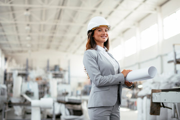 Young businesswoman with blueprint. Portrait of female architect in factory.