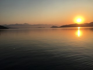 Beautiful sunset on Mediterranean ocean with mountain terrain in the background. Calm ocean no wind. 