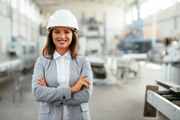 Portrait of businesswoman in factory. Young female architect with helmet in suit.	