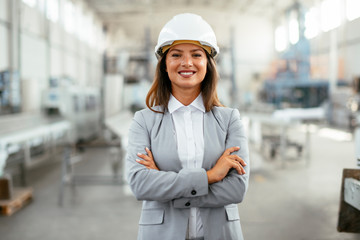 Portrait of businesswoman in factory. Young female architect with helmet in suit.	