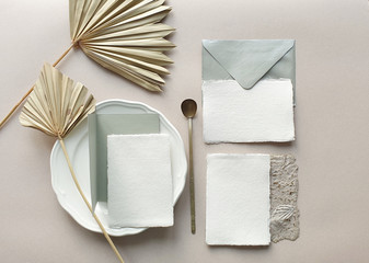 Blank white Wedding invitation cards mockups with dried palm leaf and craft envelope on textured table backgound. Elegant modern template for branding identity. Tropical design. Flat lay, top view