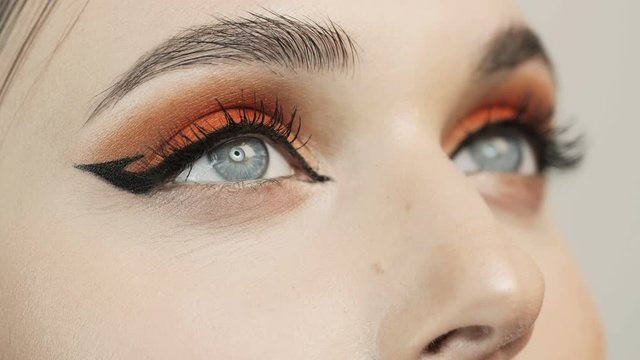 Open eyes. Close-up of girl's eyes. Narrowing of the pupils. Look up. Orange bright eyeshadows. Bright makeup. Ideal facial skin. Good eyesight.