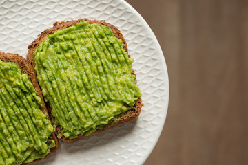 Crispy tasty fresh brown bread toast sandwiches with avocado guacomole. Tasty snack on white plate. Copy space. Top view. Idea recipe healthy diet breakfast. Source of vegetable fats for vegetarians