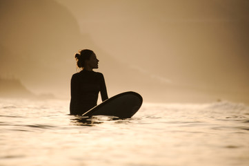 Silhouette of a surfer girl in the waters - obrazy, fototapety, plakaty