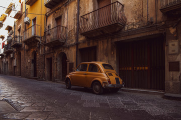 Obraz na płótnie Canvas Old orange vintage car in the street of the Ortigia island in Sicily, Italy