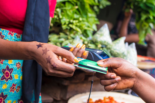 close up of an african woman selling in a local african market holding a mobile point of sale device collecting a credit card from a customer