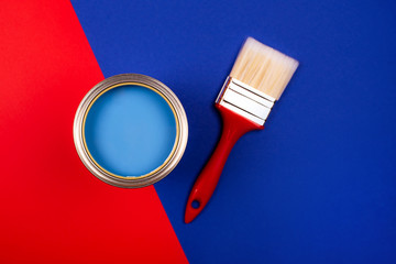 Brush with black handle on open can of teal paint on blue pastel background. Color of the year in...