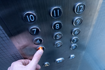 The hand presses on the first floor elevator button. A man in a metal elevator. A twelve-story building. Selective focus. Shallow depth of field. Blurry.