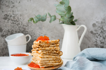Classic thin lace pancakes on a wooden plate with red caviar on a light background. A traditional dish for Shrove Tuesday