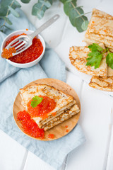 Classic thin lace pancakes on a wooden plate with red caviar on a light background. A traditional dish for Shrove Tuesday