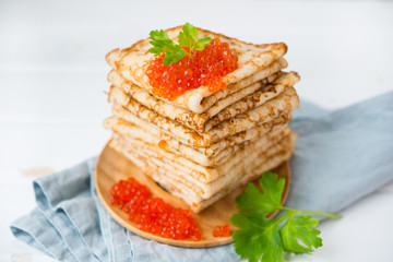 Classic thin lace pancakes on a wooden plate with red caviar on a light background. A traditional dish for Shrove Tuesday. Selective focus