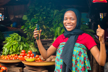 African woman selling food stuff in a cheerful local market feeling excited and happy expressing...