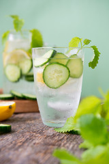 Refreshing detox water with cucumber, lemon and fresh mint on a light green background. Organic, vegan beverage.