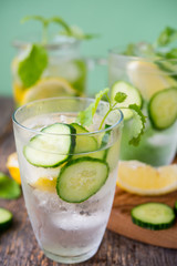 Refreshing detox water with cucumber, lemon and fresh mint on a light green background. Organic, vegan beverage.