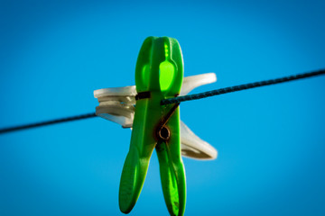 White and green clothes pegs on washing line with blue sky as background
