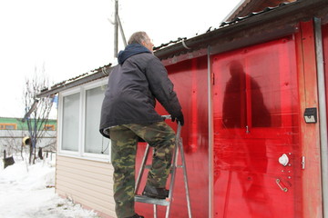 an elderly man climbed up the ladder.the pensioner wants to repair the roof of the porch at the house. © Elena Bondareva