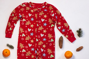 Christmas holidays sweater on white background flatlay. New year events celebration style clothes, cute red warm kids party costume, sleep and play suit. Orange tangerines and spruce cones, top view.