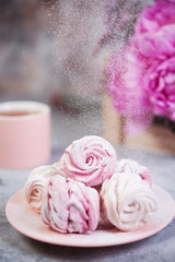 Homemade berry marshmallow in a plate is on the table with a Cup of tea. Powdered sugar falls on top of marshmallows..