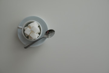 Selective focus of piles of sugar cube in white cup with spoon. Flat lay concept.