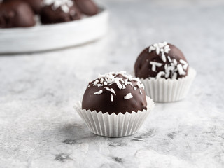 Winter dessert, healthy sugarfree peanut butter truffles covered by dark chocolate and coconut shred, christmas and new year background, fir tree branches, wooden plate, white background