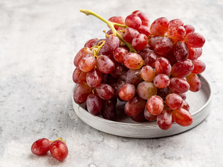 A bunch (cluster) of ripe red (purple) grapes with the drops of water on it on gray ceramic plate on light gray background. Top view. Layout t