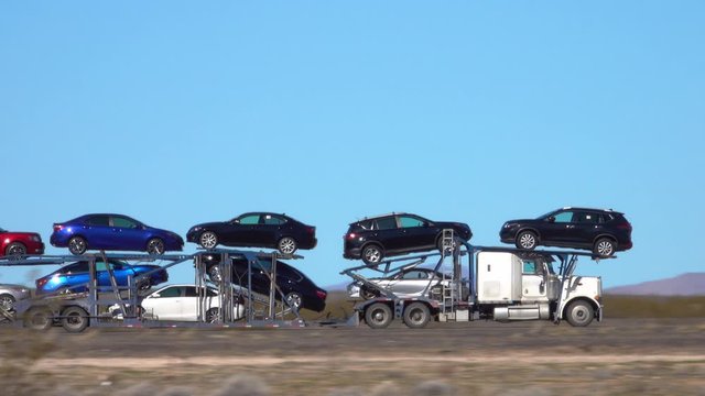 CLOSE UP Freight truck hauls cars down a highway crossing the Utah desert. Cargo lorry speeds along the interstate freeway while transporting brand new cars across the country. Hauling cars across USA