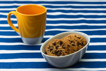 Homemade chocolate cookies in a porcelain plate and a yellow cup of coffee. Closeup.