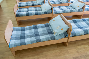 Many small beds with fresh linen in daycare preschool empty bedroom interior for comfortable afternoon nap of the kids.