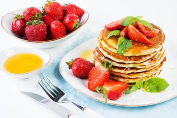 American pancakes lined with strawberries and honey poured on a white background. Classic American Breakfast.