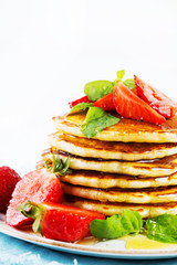 American pancakes lined with strawberries and honey poured on a white background. Classic American Breakfast.