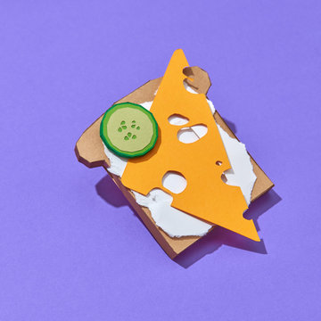 Paper handmade origami breakfast toast with cucumber slice and cheesse on a violet background. Healthy food concept.