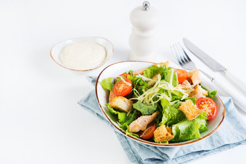 Caesar salad with chicken breast, tomatoes and wheat croutons in a plate on a white background. Horizontal photo.