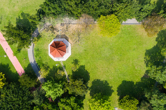 Red gazebo and trees on green grassland in park, aerial view.