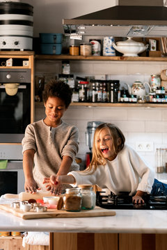Happy children with rolling pins and dough in kitchen