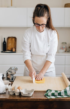 Young professional chef cutting in portion freshly made egg dough on wooden table