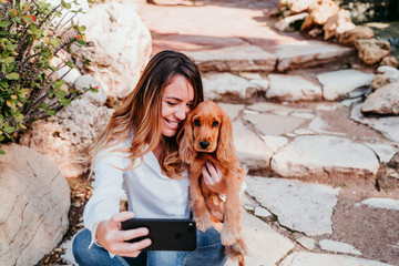 young woman taking a selfie with her cute puppy of cocker spaniel outdoors