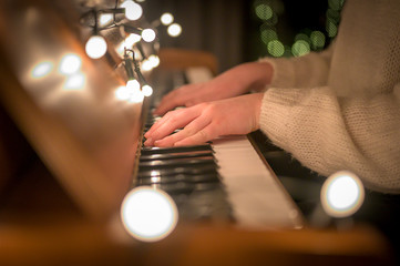 Hands of a young woman who is playing the piano, which is decorated with Christmas lights.