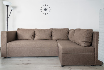 Brown sofa, floor lamp and clock on the white wall. Home interior concept