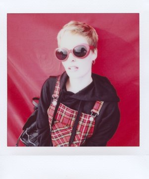 Fashionista holding strip of her hoodie on red wall.