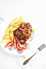 Grilled pork steak with french fries and tomatoes. Bright background. Top view. 