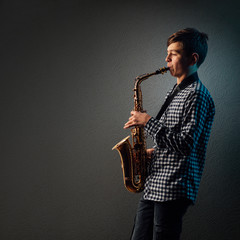 Obraz na płótnie Canvas A boy on a dark background with a searchlight plays saxophone