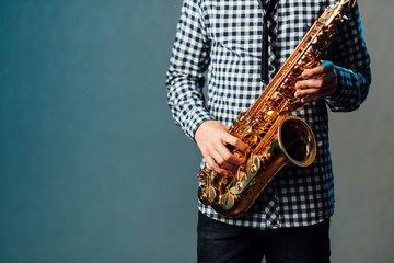 saxophone in hands close-up on blue uniform background - obrazy, fototapety, plakaty