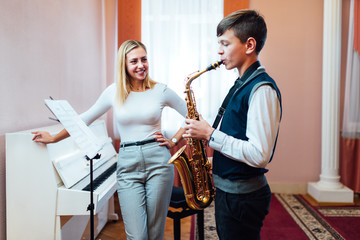 Cheerful teacher with student boy learning saxophone lessons at school